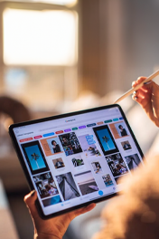A person holds a tablet and stylus, browsing a digital gallery of various images and templates.