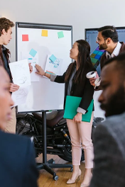 A group of people collaborates in an office, using a whiteboard with sticky notes and printed designs.