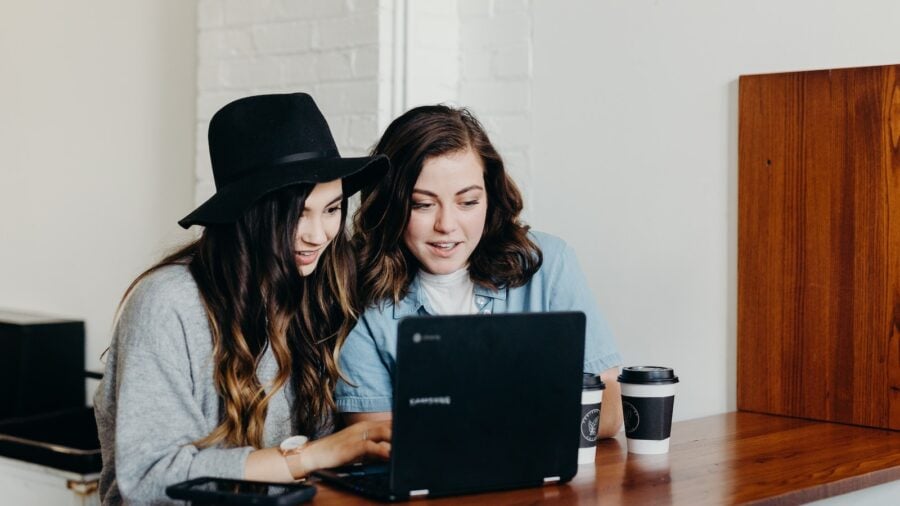 two woman sitting near table using Samsung laptop